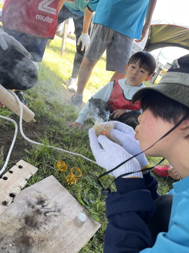 火起こし体験で煙を吹きかける小学生|春休みのアウトドア探究活動
